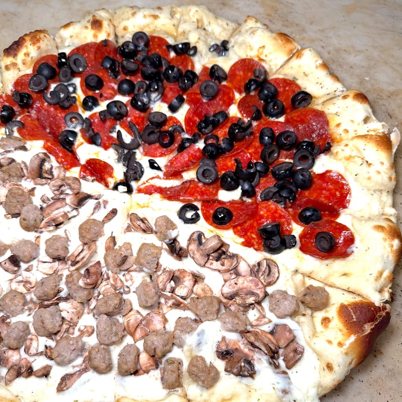 Close-up of a pizza with half pepperoni and black olives, half sausage and mushrooms.