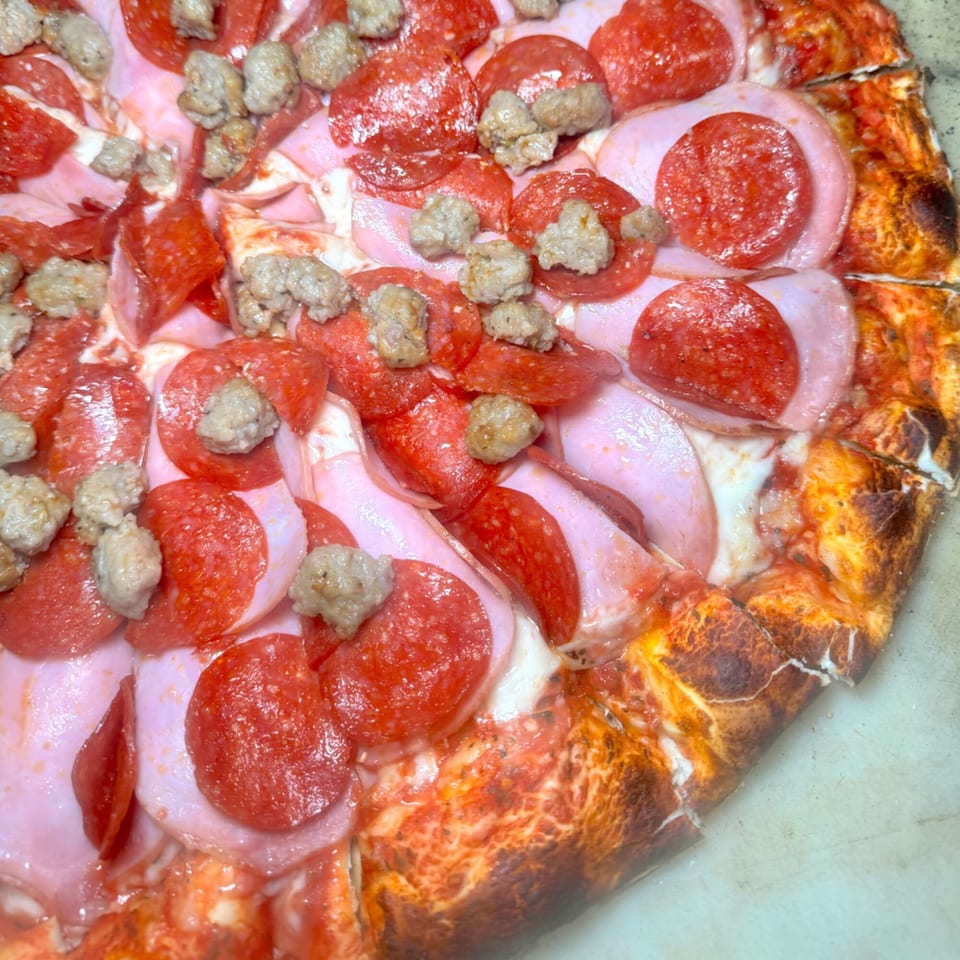 Close-up of a meat lover's pizza with pepperoni, ham, and sausage, showing a crispy crust.