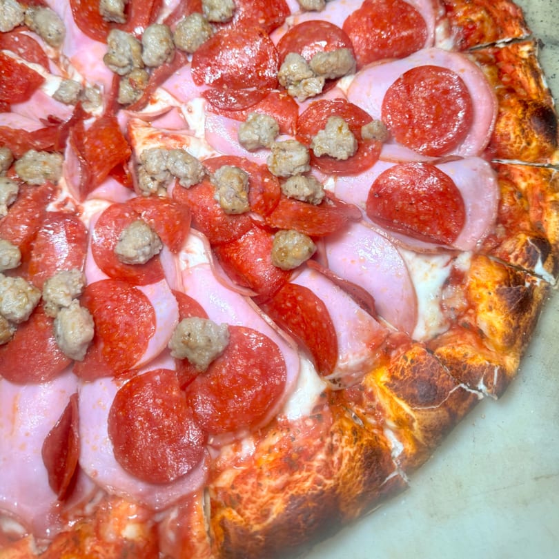 Close-up of a meat lover's pizza with pepperoni, ham, and sausage, showing a crispy crust.