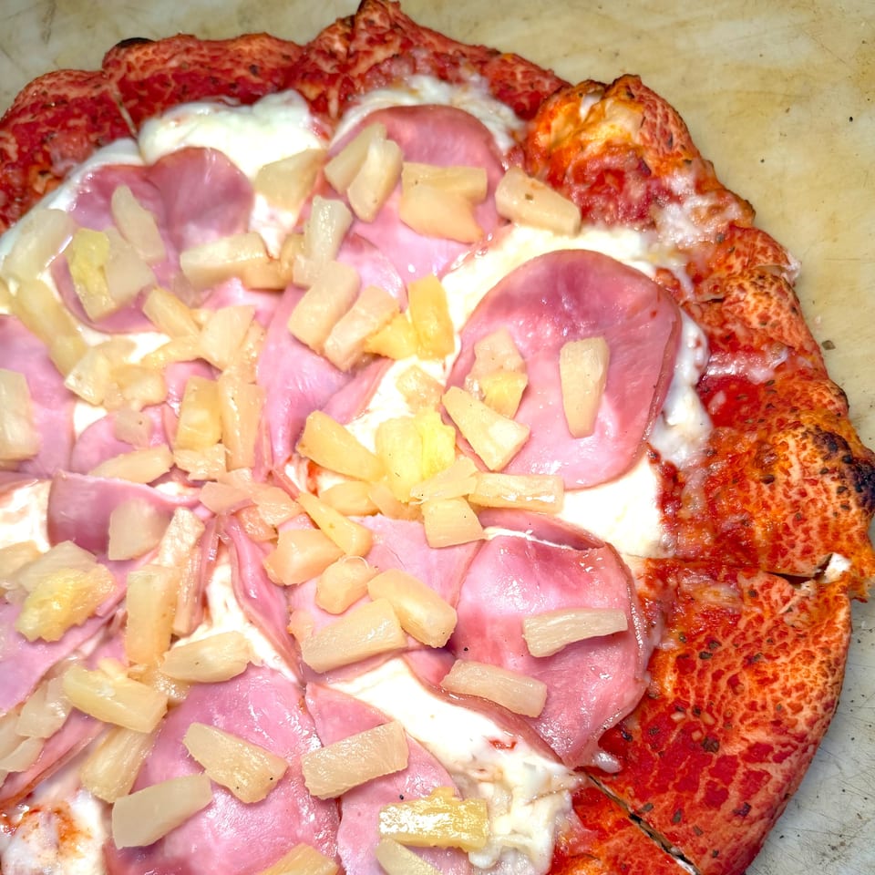 Close-up of a Hawaiian pizza with ham and pineapple on a red crust.