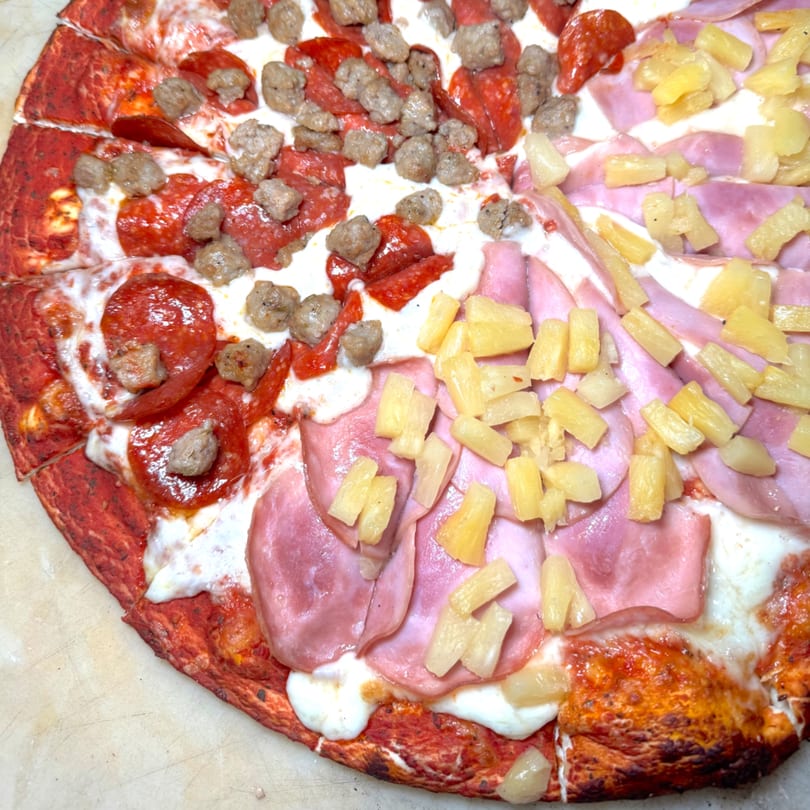 Half pepperoni and sausage pizza, half ham and pineapple pizza on a red crust.