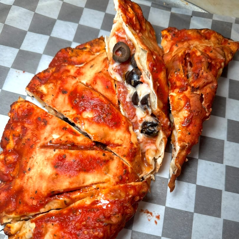 Sliced calzone with red sauce, melted cheese, and black olives on checkered paper.