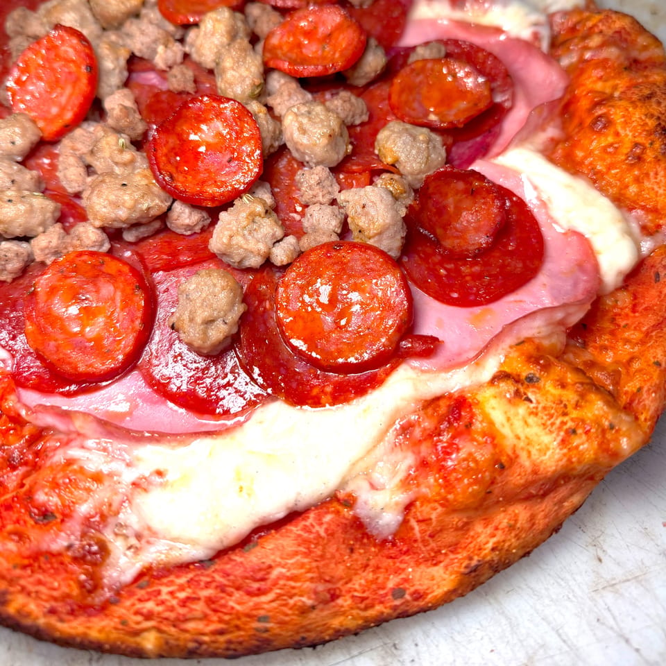 Close-up of a pizza with pepperoni, sausage, and ham, showcasing its vibrant red crust.