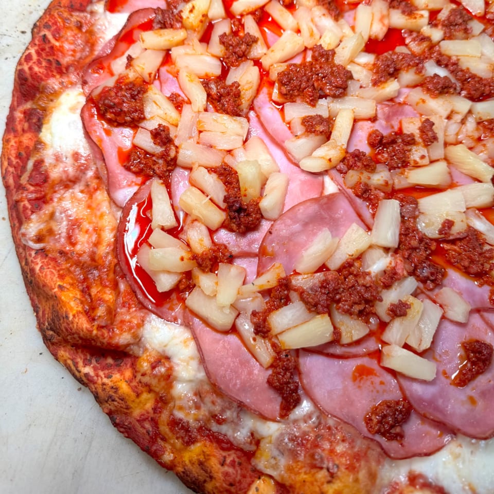 Close-up of a pizza topped with ham, pineapple chunks, and spicy chorizo sausage.