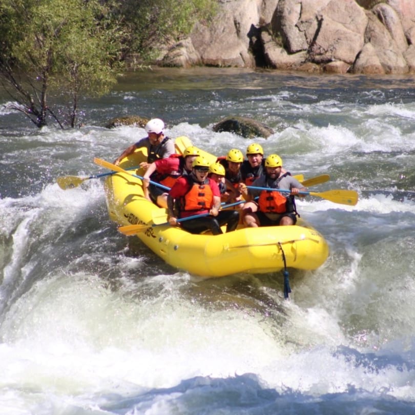 Six people in a yellow raft navigate turbulent whitewater rapids on a sunny day.