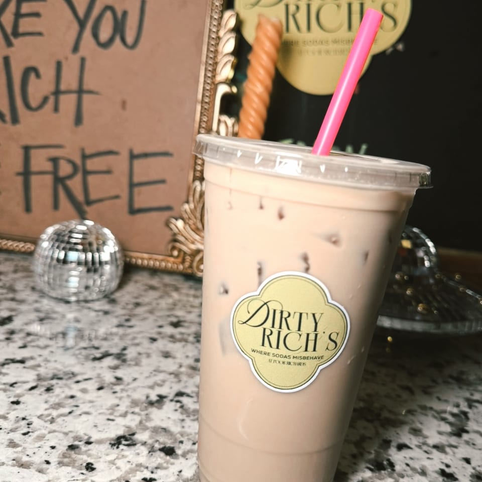 Iced Dirty Rich's drink with a pink straw on a speckled counter, with a disco ball and sign in the background.