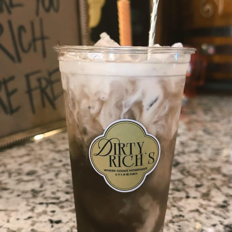 A Dirty Rich's soda with cream being poured into it, creating a swirling effect.